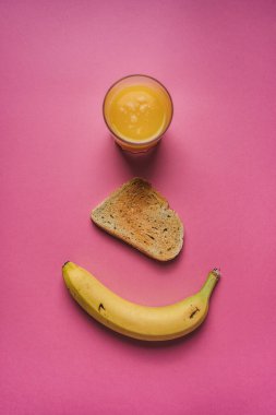 Portakal suyu bardağı, kızarmış ekmek dilimi ve pembe arka planda bir muz. Kahvaltı konsepti.
