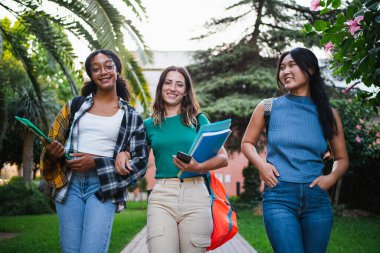 Portrait of university students looking at camera and walking in the campus holding books
