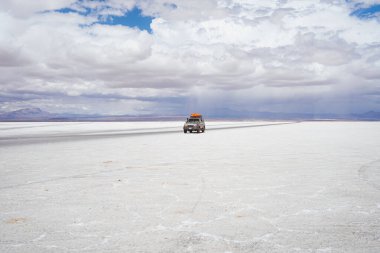 Bolivya 'da Salar de Uyuni' de arka planda yağmurlu bir arazi aracı sürüyor.