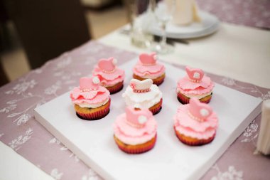 Pastel keklere yakın plan, pembe ve beyaz kremalı, inci rengi detaylar, ve süslü süslemeler, zarif bir şekilde bir tepside dizilmiş. Kutlamalar için zarif ve şık bir ikram..