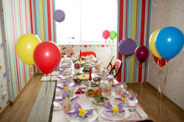 Renkli balonlar, yiyecekler ve içeceklerle süslenmiş neşeli çocuklar çizgili duvarları olan parlak bir odada..