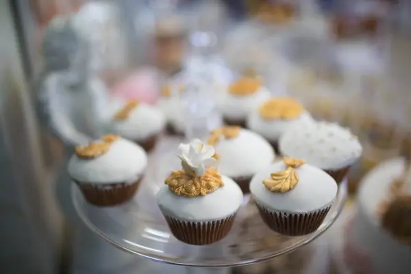 Cam bir tepside zarif bir şekilde sergilenen beyaz fondant ve altın çiçek aksanıyla süslenmiş kekler. Düğün ya da lüks parti için mükemmel..