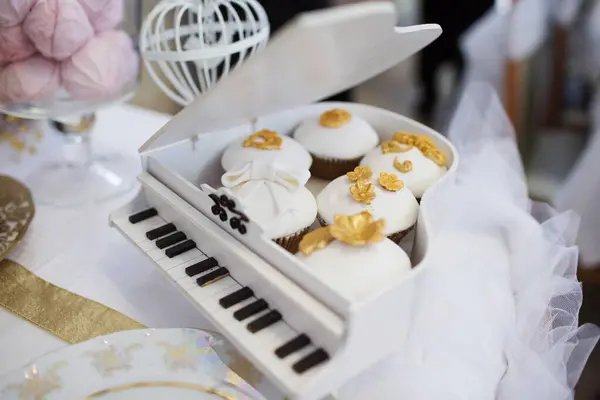 Dekoratif piyano şeklinde bir kutunun içinde düzenlenmiş beyaz ve altın keklerin yaratıcı sunumu. Eşsiz ve lüks bir düğün tatlısı gösterisi..