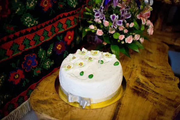Çiçek desenli beyaz pasta ahşap bir masanın üzerine yerleştirilmiş, bir buket taze çiçeğin yanına. Düğün, doğum günü ya da kutlama için zarif bir tatlı..