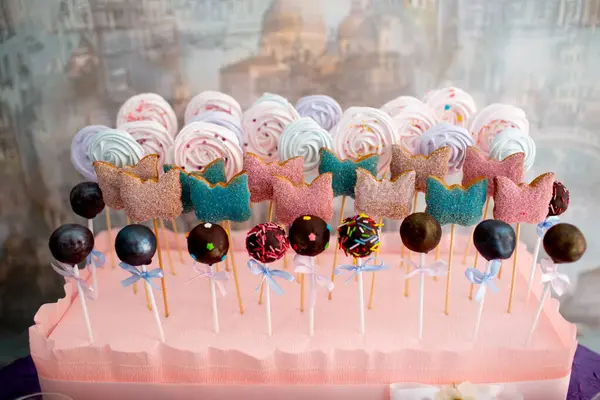 Renkli pastalar, pastalar ve çubuklar üzerinde kelebek şeklinde kurabiyeler. Doğum günü kutlaması için pembe bir stantta düzenlenmiş..