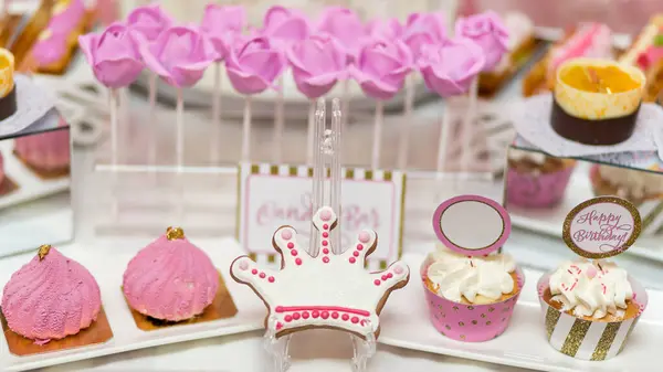 Pembe taç şeklinde kurabiyeler, kremalı kekler ve prenses temalı doğum günü partisi için mükemmel lolipop buketleri.