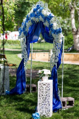 Göz kamaştırıcı düğün kemeri, beyaz ve mavi çiçeklerle süslenmiş, mavi örtüler, ve bahçeye oyulmuş zarif detaylar..