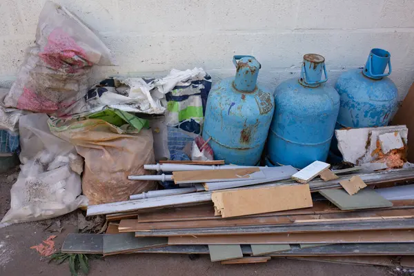 İnşaat enkazı, plastik torbalar ve beyaz bir duvara dayanmış üç eski paslı gaz silindiri. Fotoğraf, güvenli olmayan atık depolama ve çevresel tehlikeleri vurguluyor. 