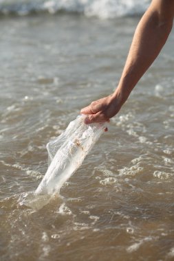 İnsan eli deniz suyundan plastik poşet topluyor, plaj temizliği kavramı, çevre bakımı ve okyanus koruması.