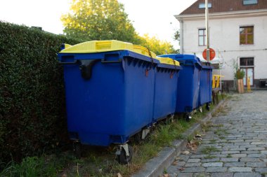 Bir kaldırım taşı sokağında sarı kapaklı mavi geri dönüşüm kutularına daha yakından bakın.