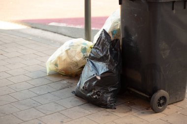 Siyah ve sarı çöp torbaları şehrin kaldırımlarındaki bir çöp kutusunun yanına konmuş..