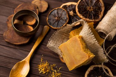 Çuval bezine sarılı sarı el yapımı sabun dilimleri ve ahşap kaşık, sade spa arka planı..