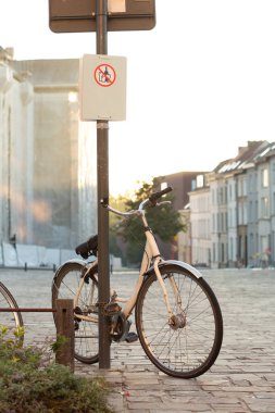 Gün batımında Avrupa şehir caddesinde yasaklı levhası olan bir direğe zincirlenmiş bisiklet..