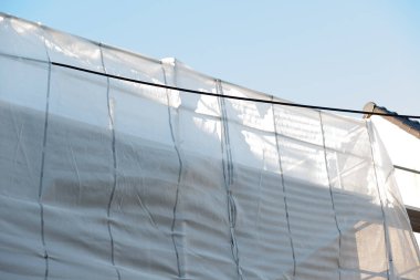 Şeffaf yenileme kumaşı ve metal iskele yapısı arka planda açık mavi gökyüzü olan bir binanın ön cephesinde..