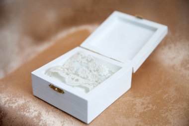 Zarif beyaz dantelli jartiyer küçük zarif bir ahşap kutunun içinde sergileniyor. Romantik gelin aksesuarı geleneği ve kadınlığı simgeliyor..