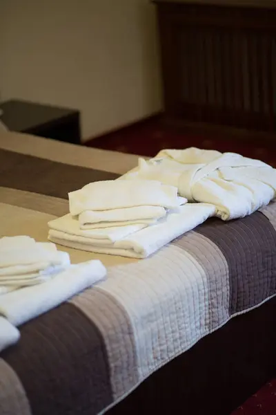 Bir yığın yumuşak beyaz havlu ve otel yatağında düzgünce yerleştirilmiş bornoz. Konukseverlik konsepti spa, sağlık, ya da konaklama reklamı.