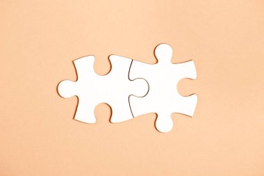 Bej arkaplanda iki adet yapboz parçası var. Takım çalışmasında doğru çözümleri bulma kavramı. 2024 yılının gösterim rengi - şeftali.