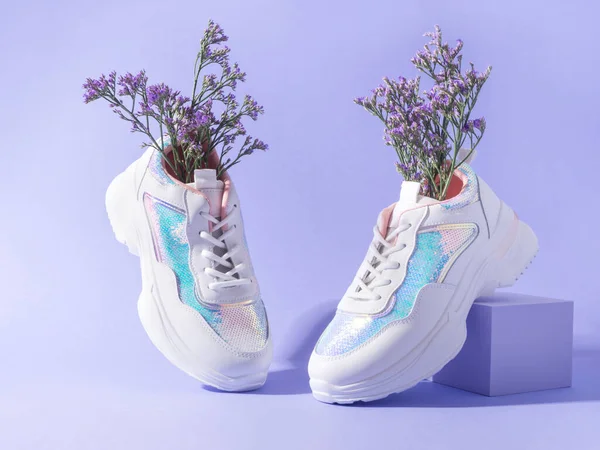 White female sneakers with sequins with flowers inside on purple background with geometric cube podium, spring summer fashion balance concept