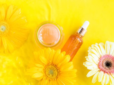 C vitamini serumu ve açık pembe krem. Suyun arka planında sarı güzel çiçekler var. Cilt bakım ürünleri düz