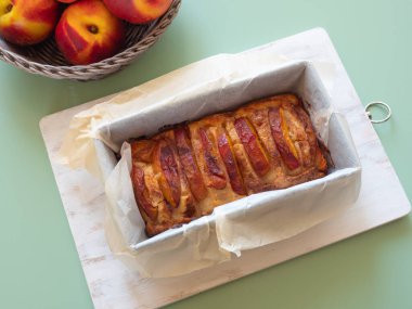 Ev yapımı vejetaryen şeftali turtası turkuaz yeşil bir açık hava masasında pişirme kalıbında. Yaz tatlı ikramı mevsimlik meyveler, üst manzara