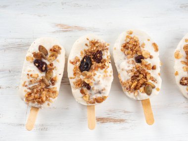 Beyaz ahşap tahtada gevrek granola ile kaplı ev yapımı Yunan yoğurtlu dondurma. Şekersiz sağlıklı yaz atıştırması