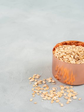 Tam tahıllı organik yulaf ezmesi, gri arka planda, ahşap tahtanın üzerinde ölçü kabında.