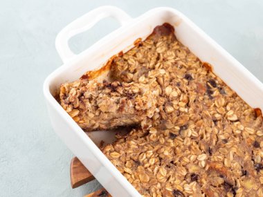 Turkuaz arka planda beyaz tavada vejetaryen yulaflı muzlu kek. Yuvarlak yulaf, muz, fıstık ezmesi, soya sütü ve çikolata parçacıklı sağlıklı kahvaltı turtası.