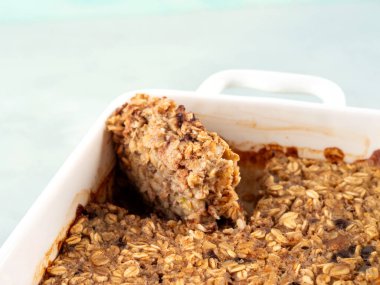 Turkuaz arka planda beyaz tavada vejetaryen yulaflı muzlu kek. Yuvarlak yulaf, muz, fıstık ezmesi, soya sütü ve çikolata parçacıklı sağlıklı kahvaltı turtası. Yakın çekim.