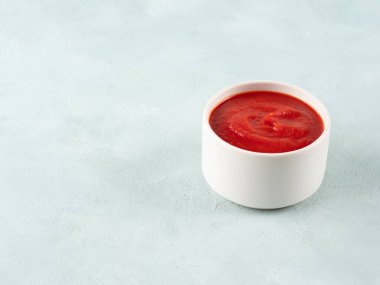 Açık mavi arka planda beyaz kasede domates püresi sosu..