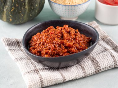 Ev yapımı vejetaryen balkabağı domatesli bolonez ragusu, açık mavi arka planda mutfak havlusunda siyah kâsede soya proteini granülleri. Sebzeli ve soya fasulyeli lezzetli sonbahar makarna sosu, yakın plan.