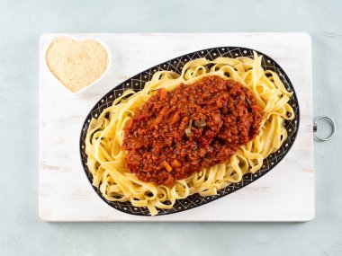 Tagliatelle pasta with vegan tomato bolognese ragu with soya protein granules on white wooden board on turquoise background. clipart