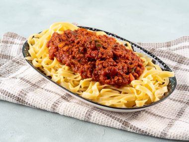 Tagliatelle makarnası vejetaryen domatesli bolonez ragu ve açık mavi arka planda mutfak havlusu bezinde soya proteini granülleri..