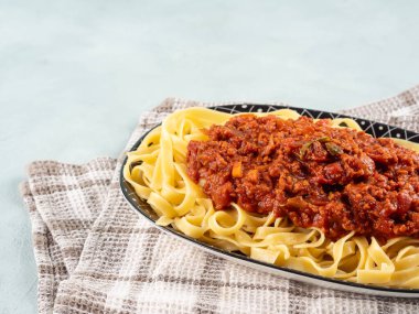 Tagliatelle makarnası vejetaryen domatesli bolonez ragu ve açık mavi arka planda mutfak havlusu bezinde soya proteini granülleri..