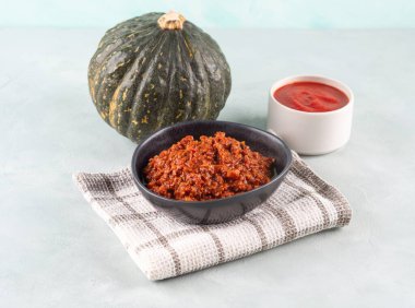 Ev yapımı vejetaryen balkabağı domatesli bolonez ragusu, açık mavi arka planda mutfak havlusunda siyah kâsede soya proteini granülleri. Sebzeli ve soya fasulyeli kışın lezzetli makarna sosu.
