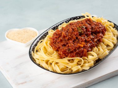 Tagliatelle makarnası vejetaryen domates bolonez ragu ve soya proteini granülleri beyaz tahta üzerinde turkuaz arka planda..