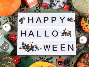 Yeşil arka planda ışık kutusunda Cadılar Bayramı 'nız kutlu olsun. Dekor ve balkabaklarıyla. Tatil çocukları içki niyetine şeker ve fincanlarla parti konsepti