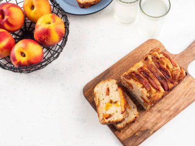 Beyaz masadaki tahta kesme tahtasının üzerinde ev yapımı şeftalili şeftalili turta dilimleri. Mevsimlik meyveli yaz pastası