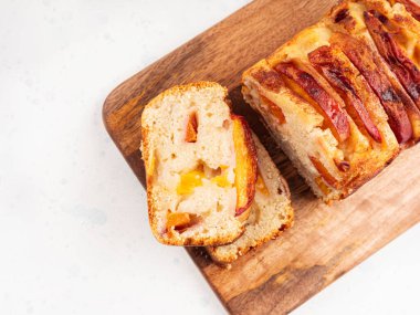 Beyaz masadaki tahta kesme tahtasının üzerinde ev yapımı şeftalili şeftalili turta dilimleri. Mevsimlik meyveli yaz pastası