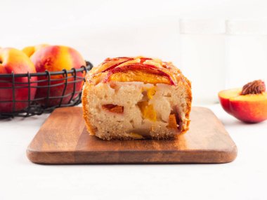 Beyaz masadaki tahta kesme tahtasının üzerinde ev yapımı şeftalili şeftalili turta. Mevsimlik meyveli yaz pastası