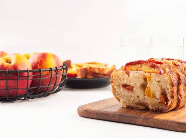 Beyaz masadaki tahta kesme tahtasının üzerinde ev yapımı şeftalili şeftalili turta. Mevsimlik meyveli yaz pastası