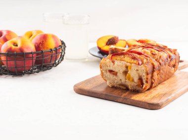 Beyaz masadaki tahta kesme tahtasının üzerinde ev yapımı şeftalili şeftalili turta. Mevsimlik meyveli yaz pastası