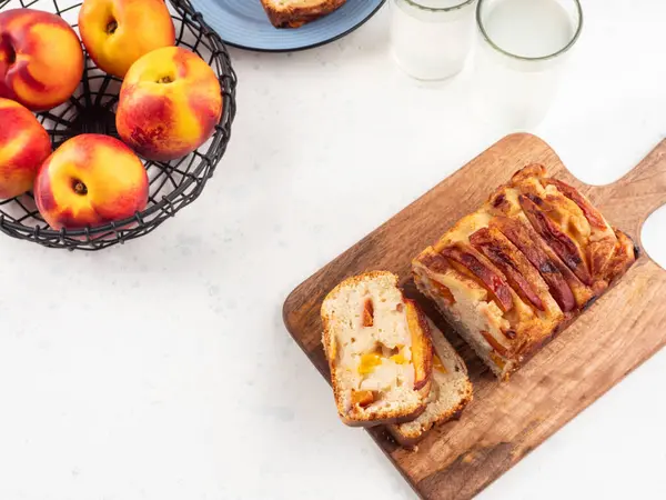 Beyaz masadaki tahta kesme tahtasının üzerinde ev yapımı şeftalili şeftalili turta dilimleri. Mevsimlik meyveli yaz pastası