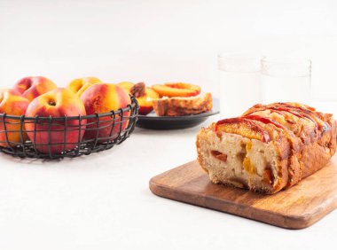 Beyaz masadaki tahta kesme tahtasının üzerinde ev yapımı şeftalili şeftalili turta. Mevsimlik meyveli yaz pastası