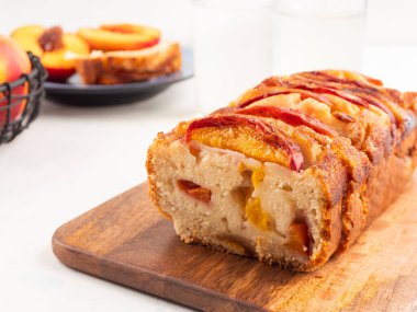 Beyaz masadaki tahta kesme tahtasının üzerinde ev yapımı şeftalili şeftalili turta. Mevsimlik meyveli yaz pastası