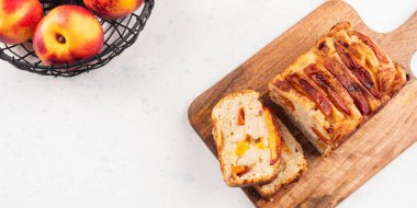 Beyaz masadaki tahta kesme tahtasının üzerinde ev yapımı şeftalili şeftalili turta dilimleri. Mevsimlik meyveli yaz pastası