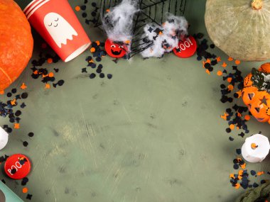 Cadılar Bayramı yeşil arka planda balkabağı ve parti dekoruyla düzüşme. Tatil çocukları içki niyetine şeker ve fincanlarla parti konsepti