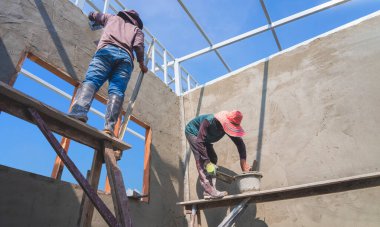 Ahşap iskeledeki iki Asyalı inşaat işçisinin düşük açılı görüntüsü inşaat alanındaki beton duvarı sıvamış.