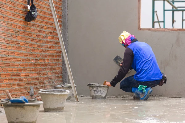 Rear side view of Asian builder using trowel to polishing concrete wall in house construction site