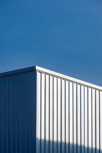 Corrugated Steel Warehouse Building Wall with Sunlight Reflection on surface against Blue Clear Sky Background in Vertical Frame