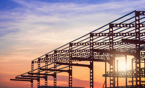 Silhouette of castellated beam metal structure of large industrial building in construction site against sunset sky background
